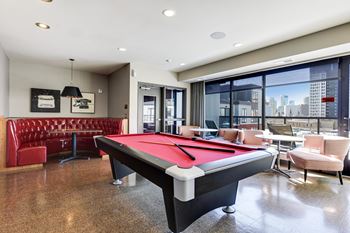 Billiards table in the center of the community club room with a red booth in the corner and large windows to the right.